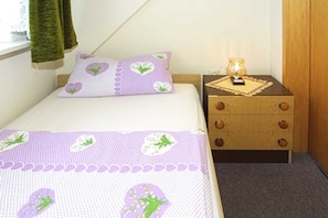 Une chambre à coucher avec un lit, une table de chevet dotée de tiroirs, une lampe et une fenêtre avec des rideaux.