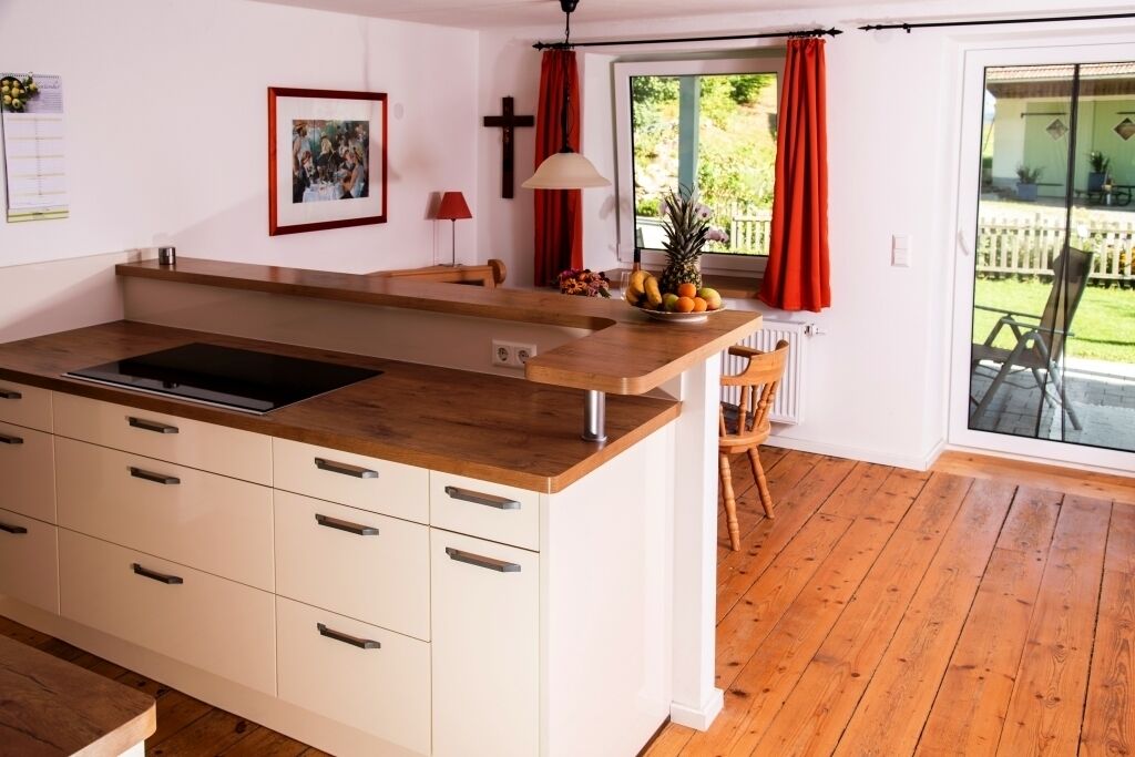 A modern kitchen with wooden countertops, white cabinets, and a large window with red curtains.