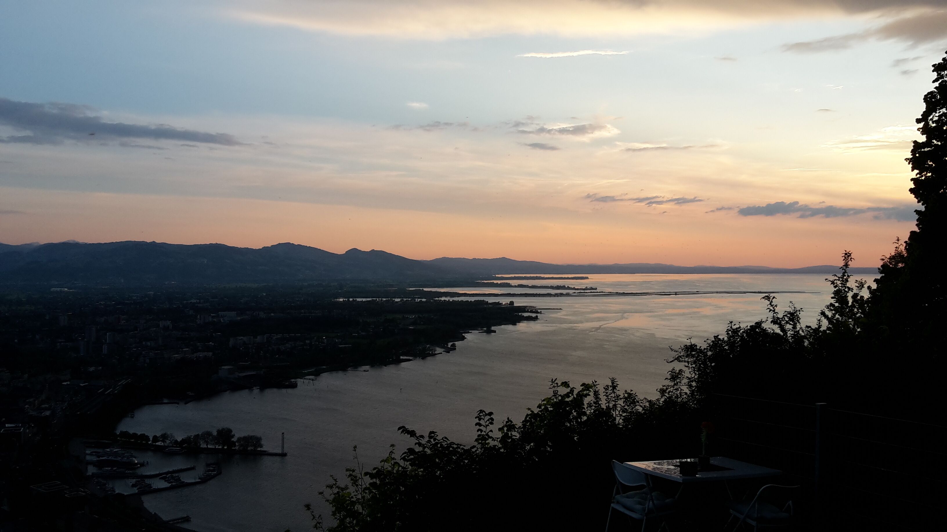 A panoramic view of a river with mountains in the background and a cityscape along the riverbanks.
