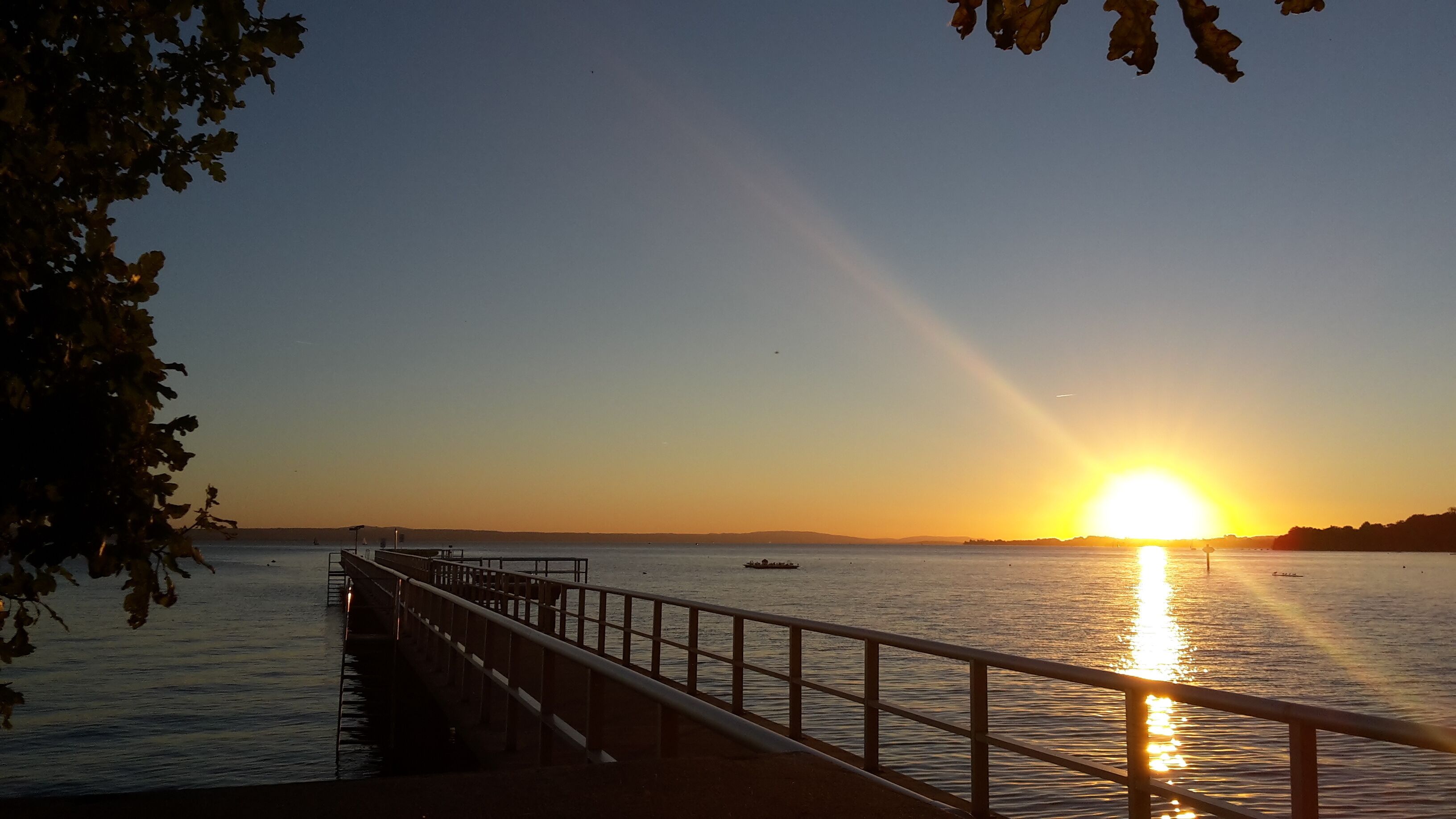Een steiger die zich uitstrekt over rustig water, met een zonsondergang op de achtergrond.