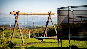 Un conjunto de columpios de madera en un área con césped, una cerca de malla y vistas a montañas distantes.