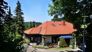 A house with a red-tiled roof, surrounded by greenery and trees. - Modern, bright and quiet apartment in the heart of the Black Forest (Sankt Märgen)