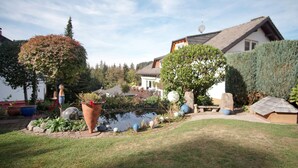 A garden with a pond, potted plants, and a house with a sloped roof. - Modern, bright and quiet apartment in the heart of the Black Forest (Sankt Märgen)