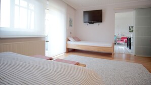 A bedroom with a bed, a TV mounted on the wall, a bedside table, and a door leading to another room. - Modern, bright and quiet apartment in the heart of the Black Forest (Sankt Märgen)