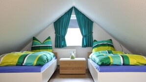 Ein kleines, dreieckiges Schlafzimmer im Dachgeschoss mit zwei Betten und passender Bettwäsche in Grün- und Gelbtönen sowie einem Nachttisch in der Mitte.
