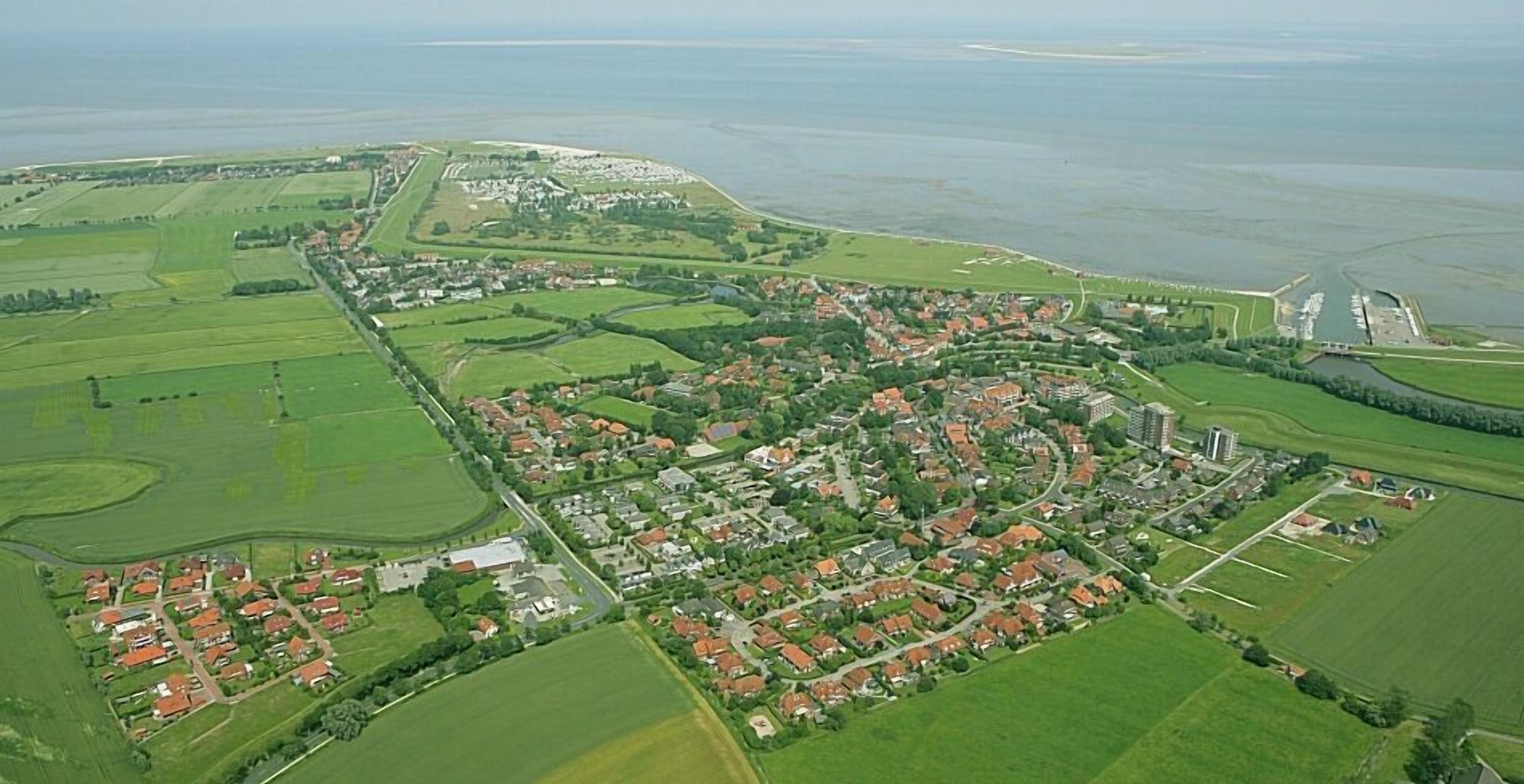Vista aérea de un pueblo costero con zonas residenciales, campos verdes y un puerto deportivo.