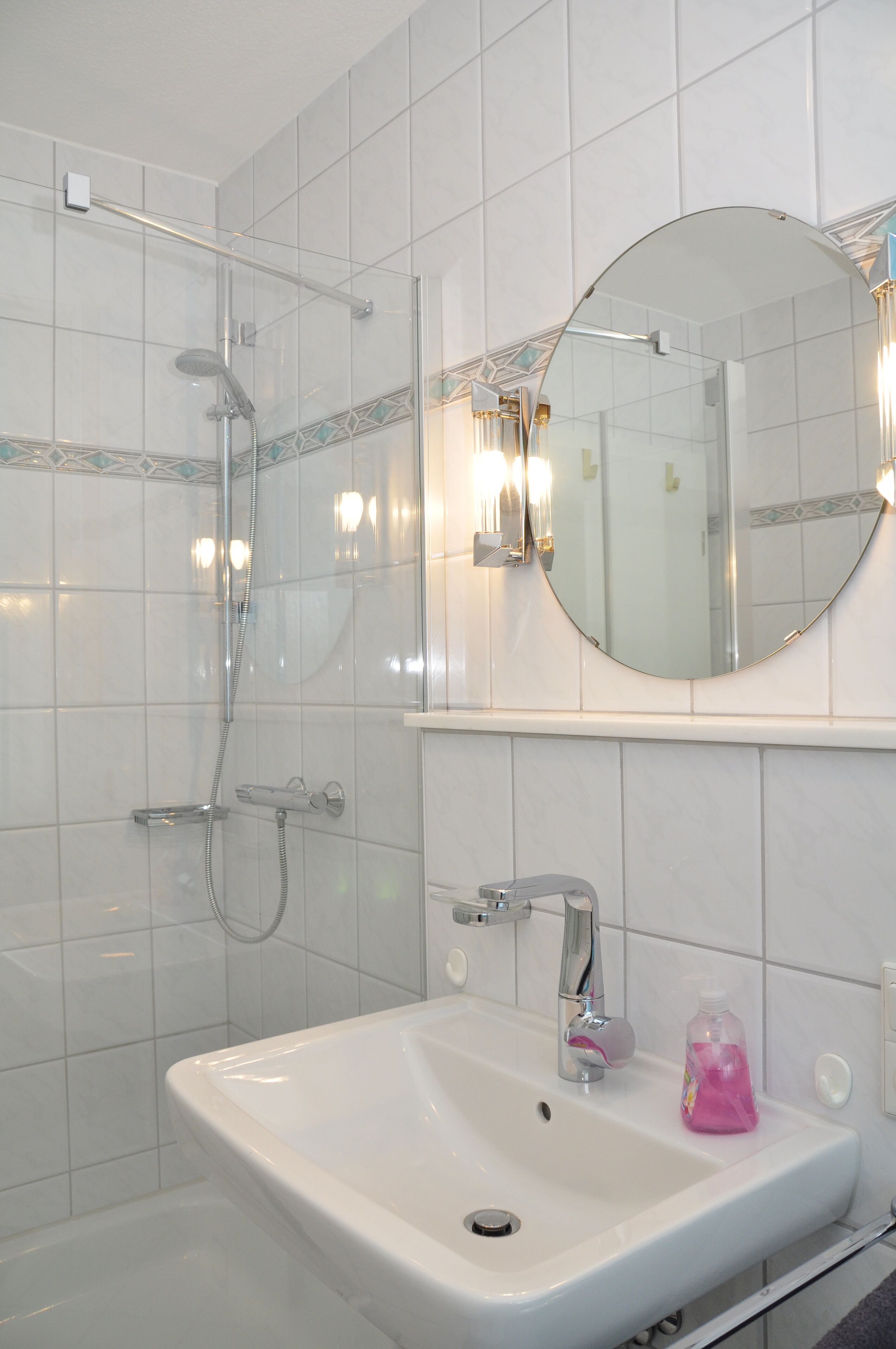 Un baño con lavamanos blanco, un espejo redondo y ducha con mampara de vidrio.