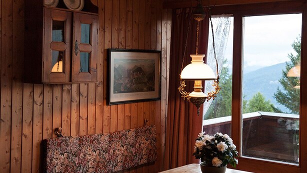 Un interior de madera con un banco, un mueble con puertas de cristal, un cuadro enmarco y una mesa con un florero.