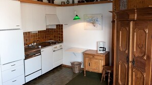 Cocina compacta con armarios blancos, estufa y lavamanos. Se observa un mueble de madera con una cafetera encima.