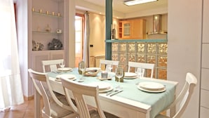 Zona pranzo con tavolo apparecchiato per quattro persone, sedie bianche e tovaglia azzurra.