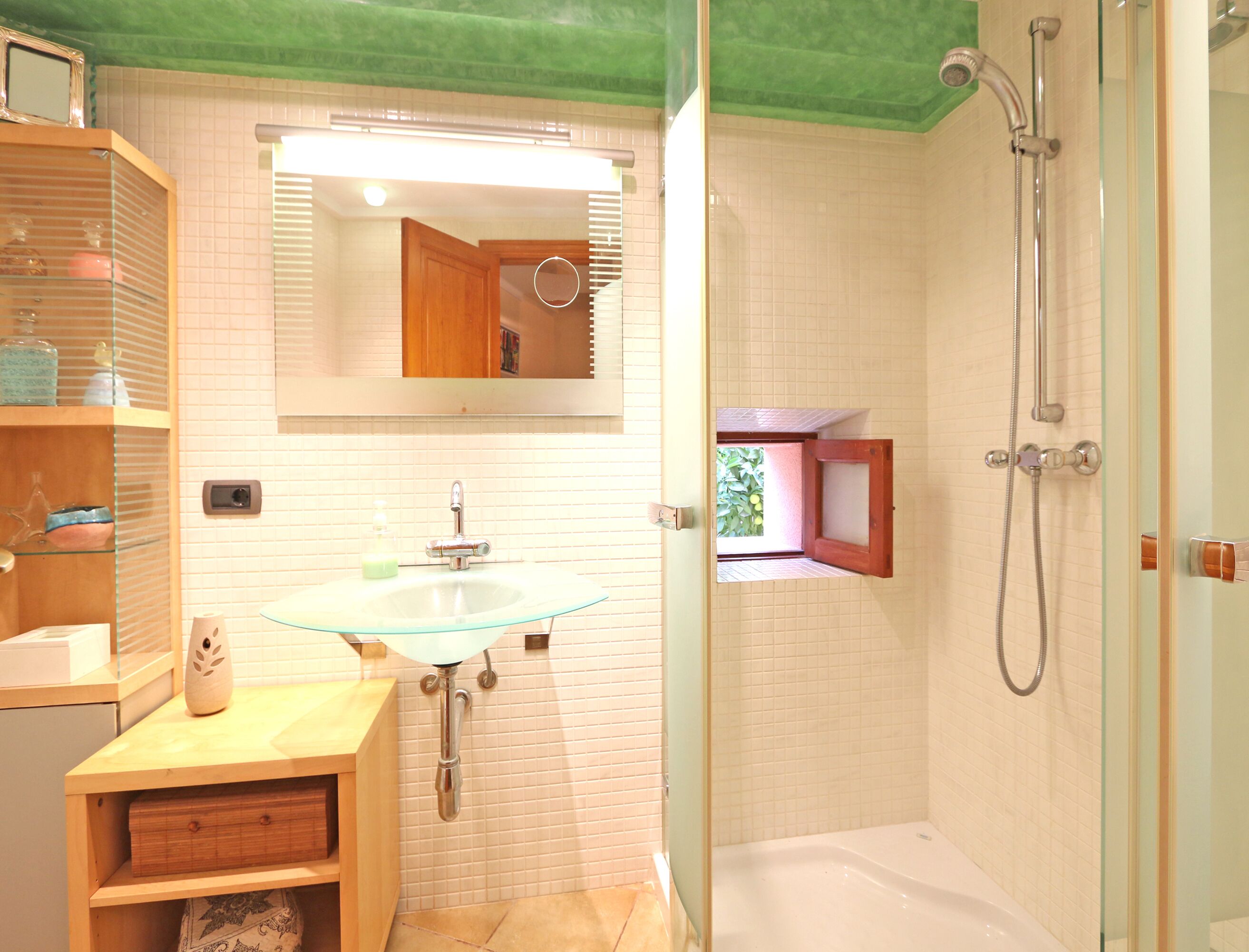 Un baño con lavamanos de vidrio, tocador de madera, espejo y zona de ducha.