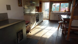 A kitchen with wooden cabinets, a stove, and a dining area with a table and chairs. - self-catering holiday house (about 130m²), ideal for 2-3 families (Blons)