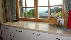 A kitchen with a large window, wooden cabinets, and a view of a wooden fence and mountains. - self-catering holiday house (about 130m²), ideal for 2-3 families (Blons)