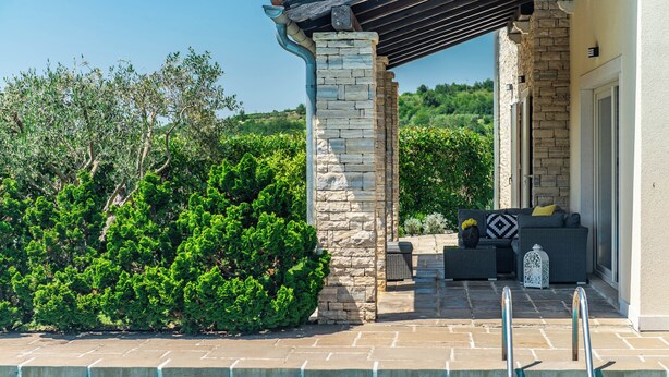 A pool area with stone pillars, a covered seating area, and lush greenery.