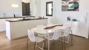 Une cuisine moderne avec des meubles blancs, un îlot central et un coin repas avec des chaises blanches.
