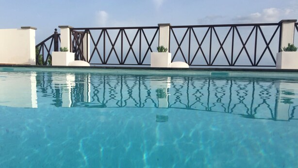 Une piscine à l’eau d’un bleu cristallin, entourée d’un mur blanc et d’une clôture en métal noir.