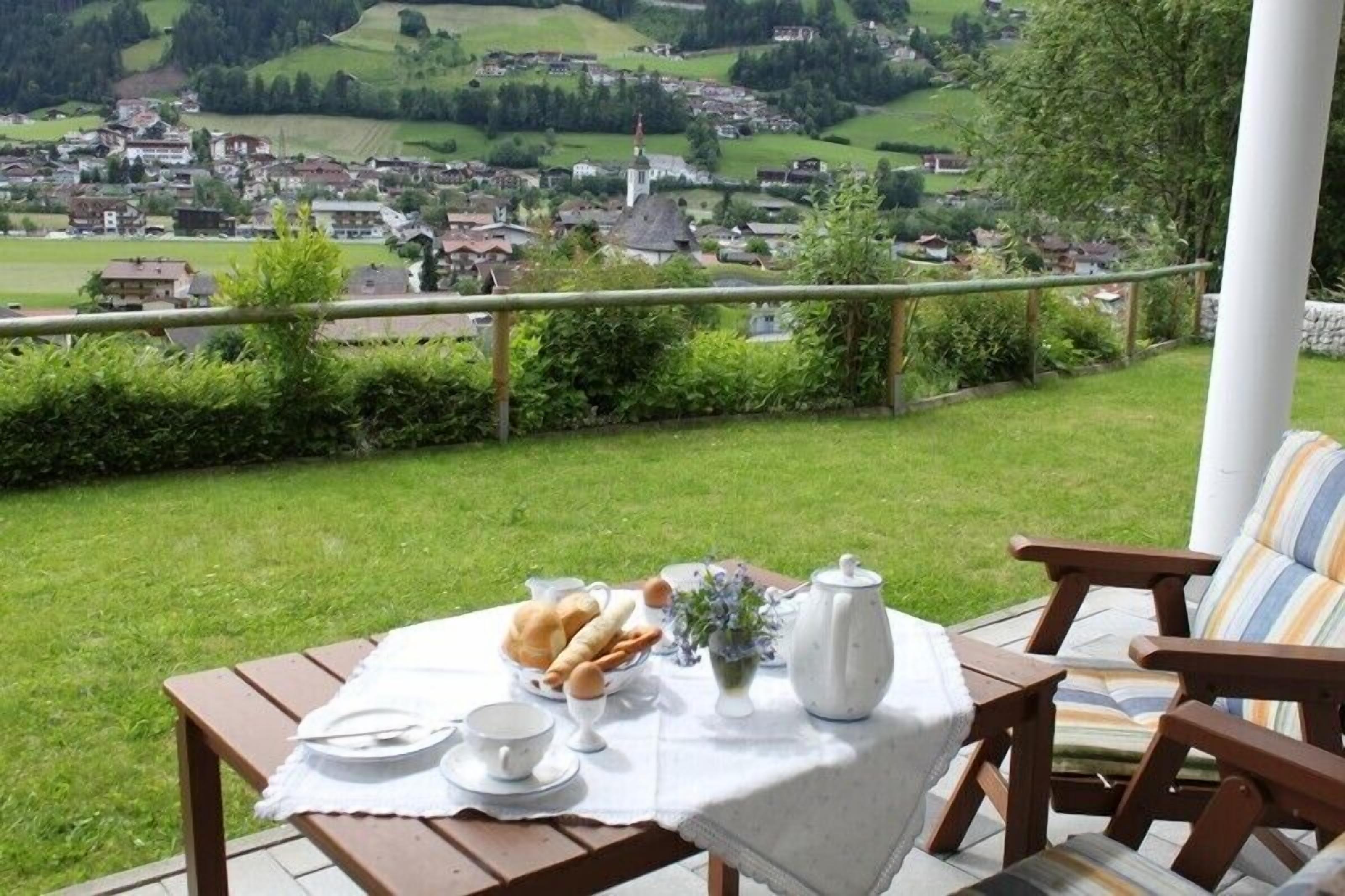 A patio with a table set for breakfast, overlooking a village.