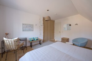 A bedroom with a large bed, a chair, a bench, a desk, a wardrobe, and a hanging light fixture. - generous thatched cottage (160 m²) on the Baltic Sea, sauna, stove, forest edge location (Rerik)