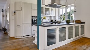 A modern kitchen with white cabinets, a central island with a sink, and a large window providing natural light. - generous thatched cottage (160 m²) on the Baltic Sea, sauna, stove, forest edge location (Rerik)
