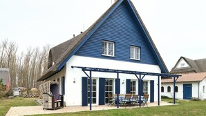 A house with a blue exterior, a thatched roof, and a covered patio area with outdoor furniture. - generous thatched cottage (160 m²) on the Baltic Sea, sauna, stove, forest edge location (Rerik)