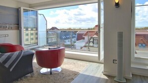A modern living room with a large sliding glass door leading to a balcony, a red chair, and a sofa. - WoogeDiva - the highest apartment on Wangerooge (Wangerooge)