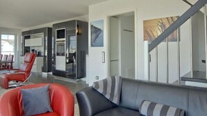 A modern living room with a grey sofa, red chairs, and a staircase. - WoogeDiva - the highest apartment on Wangerooge (Wangerooge)