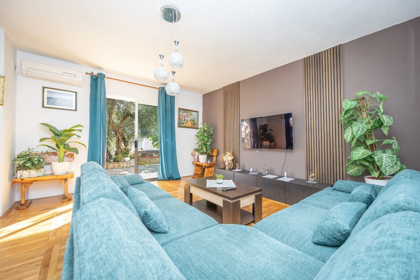 A modern living room with a sofa set, a coffee table, a TV, and potted plants.