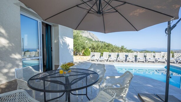 Un espace aménagé au bord de la piscine, avec une table, des chaises et un parasol.