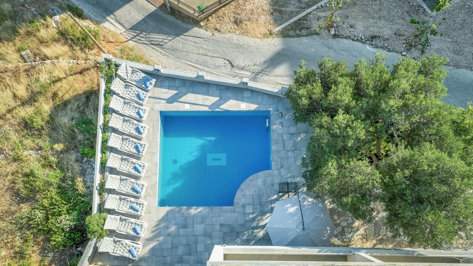 Vue aérienne d’une piscine avec des chaises longues et une terrasse en pierre.