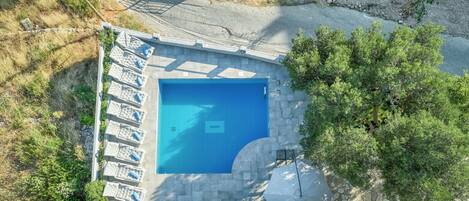Vue aérienne d’une piscine avec des chaises longues et une terrasse en pierre.