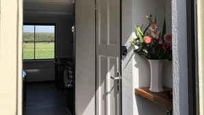 A hallway with a door leading to a room, a window with a view of a field, and a shelf with a vase of flowers. - Nature house near Amsterdam Peace and beautiful view of private rental (Breukelen)