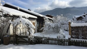 Een besneeuwd woongebied met huizen, een houten omheining en een berg op de achtergrond.