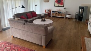 Een woonkamer met een grijze bank, een ronde salontafel, een wit kastje en een schilderij van een rode bloem.