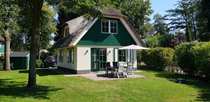 A green house with a thatched roof, a patio with outdoor furniture, and a car parked nearby. - Salland Vakantie Heeten (Heeten)