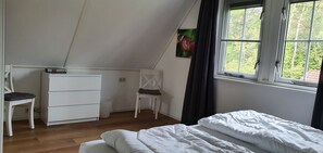 A bedroom with a bed, a chair, a desk, and a window with a view of trees. - Salland Vakantie Heeten (Heeten)