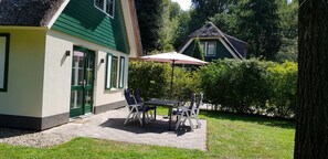 A patio with a table and chairs, a thatched-roof house in the background, and a well-maintained garden. - Salland Vakantie Heeten (Heeten)