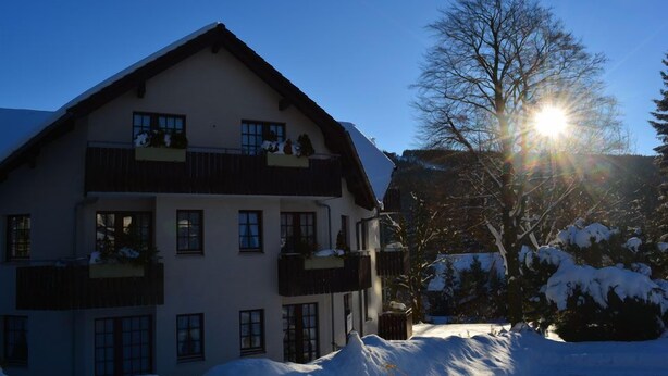 A multi-story building with balconies, surrounded by snow-covered trees and a clear sky. - Hoffmann's apartment in the residence Bocksbergblick (Goslar)