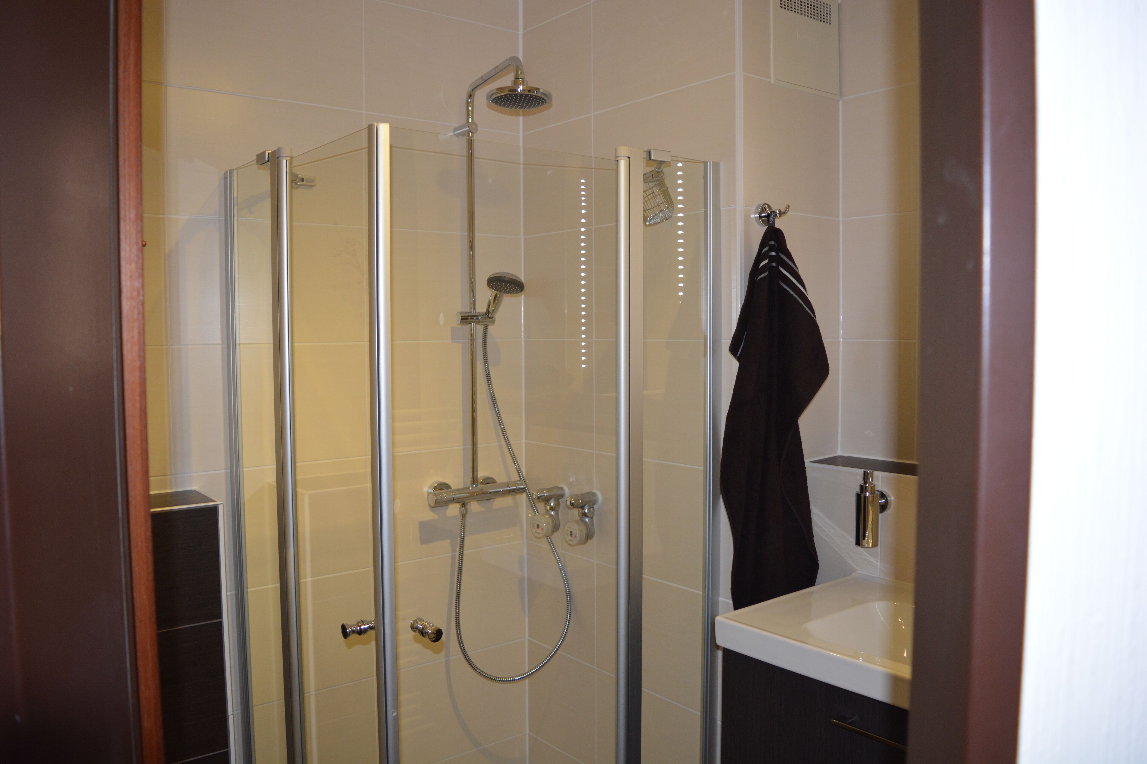 A glass-enclosed shower with a handheld showerhead and a wall-mounted faucet.