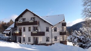 A multi-story building with balconies, surrounded by snow-covered trees and a mountainous backdrop. - Hoffmann's apartment in the residence Bocksbergblick (Goslar)