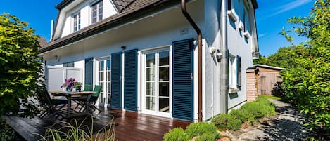 A two-story house with a wooden deck, a patio table with chairs, and a garden with rocks and plants.