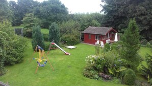 A red house with a small deck and a swing set in a lush garden.