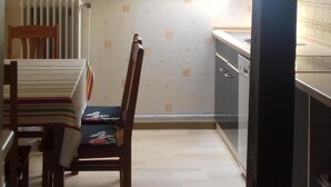 A small kitchen with a window, a radiator, and a dining area with chairs and a table.