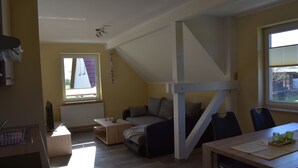 A compact living space with a loft bed, a sofa, a dining table, and a window providing natural light.
