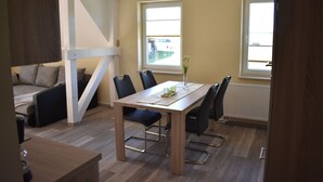 A modern living room with a wooden dining table, black chairs, a sofa, and a window with a view.