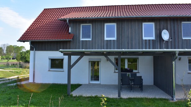 A two-story house with a red-tiled roof, a covered patio with outdoor furniture, and a satellite dish.