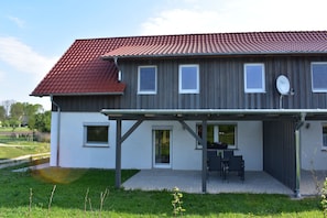 A two-story house with a red-tiled roof, a covered patio with outdoor furniture, and a satellite dish.