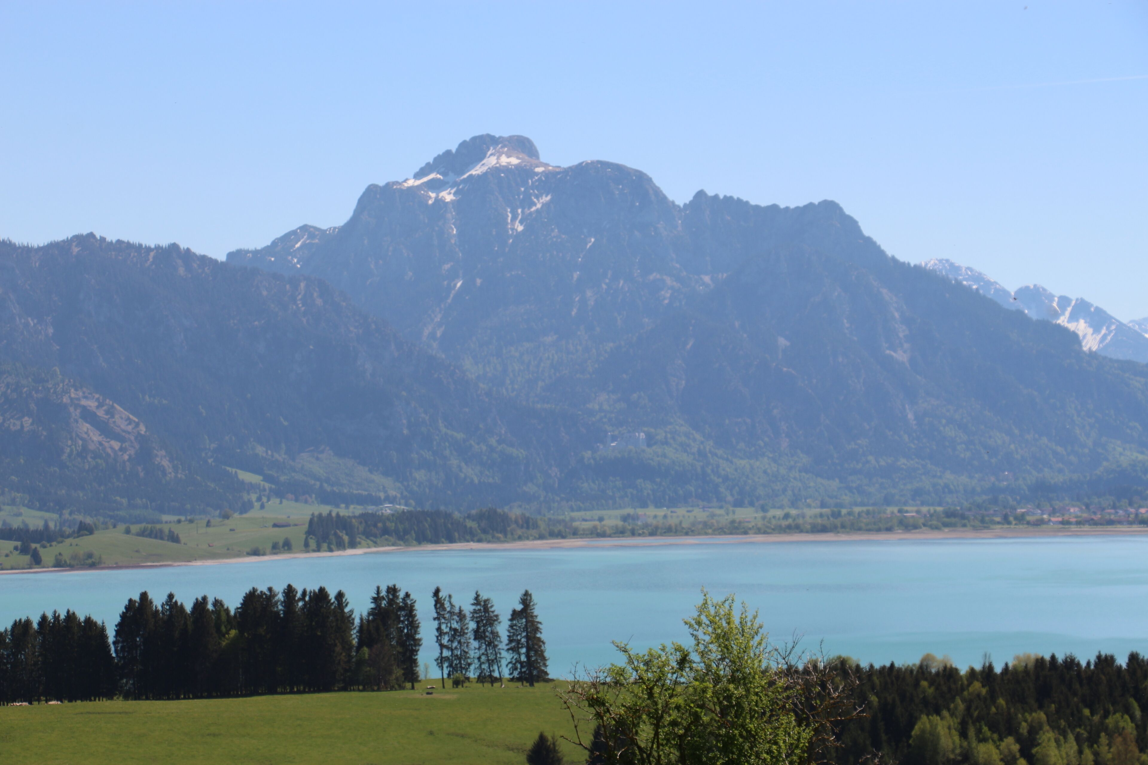 Un paysage montagneux avec un lac et une zone boisée au premier plan.