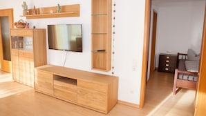 A modern living room with a wooden entertainment unit, a flat-screen TV, and a bed with a wooden headboard. - Quiet, TV, WiFi, terrace, lake, parking (Füssen)
