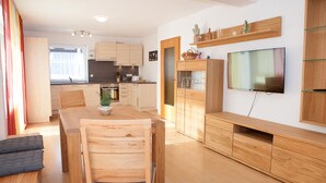 A modern kitchen with wooden cabinets, a dining area with a wooden table and chairs, and a TV mounted on the wall. - Quiet, TV, WiFi, terrace, lake, parking (Füssen)