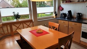 Een compacte keuken met een eethoek, met een houten tafel, stoelen en uitzicht door de ramen.